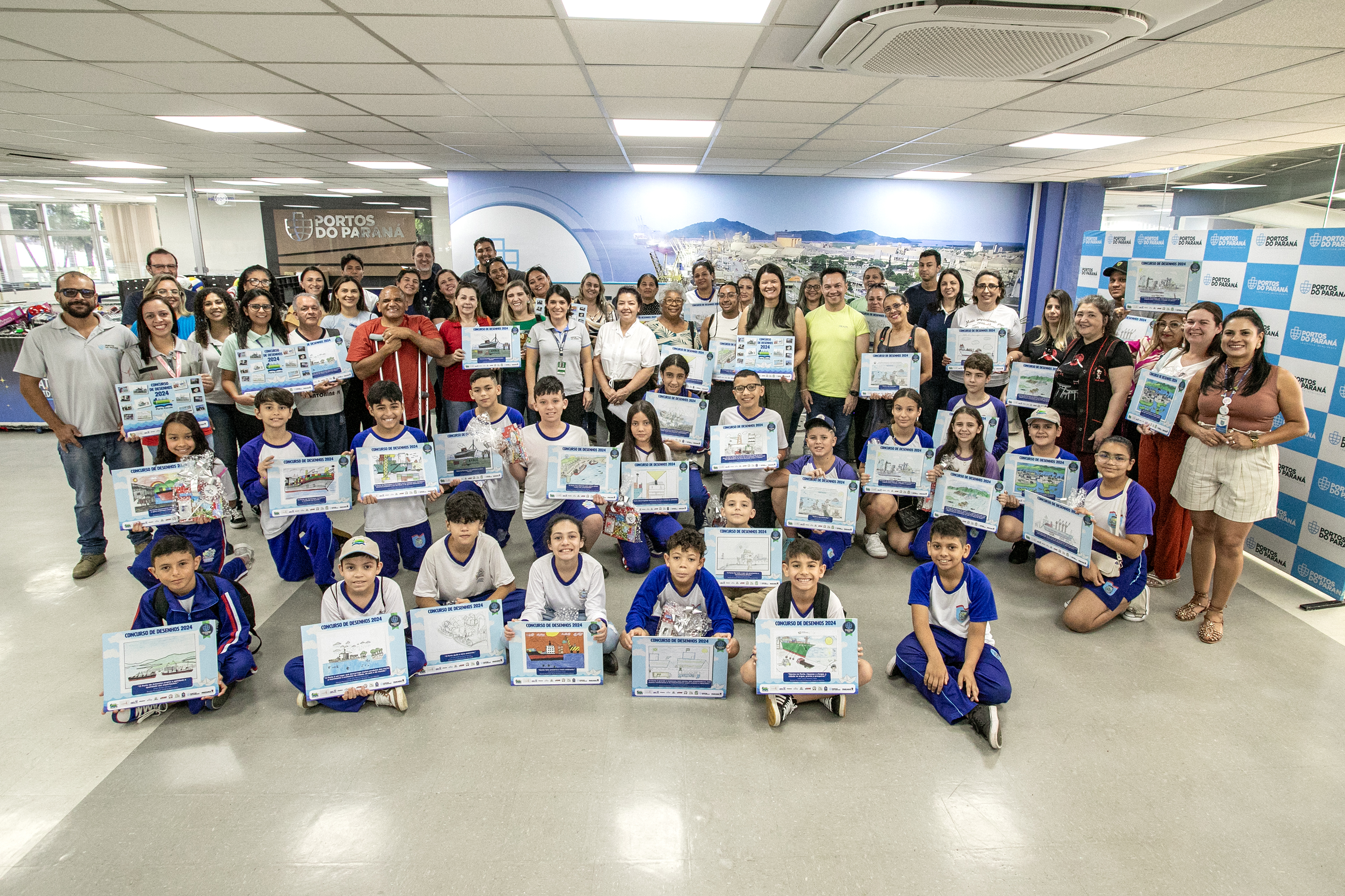 #praquemnaopodever Na recepção da Portos do Paraná, dezenas de crianças estão posicionadas segurando uma placa em homenagem ao prêmio do Concurso de Desenho do Porto Escola. Professores, pais, representantes dos municípios e da Portos do Paraná também estão na foto.