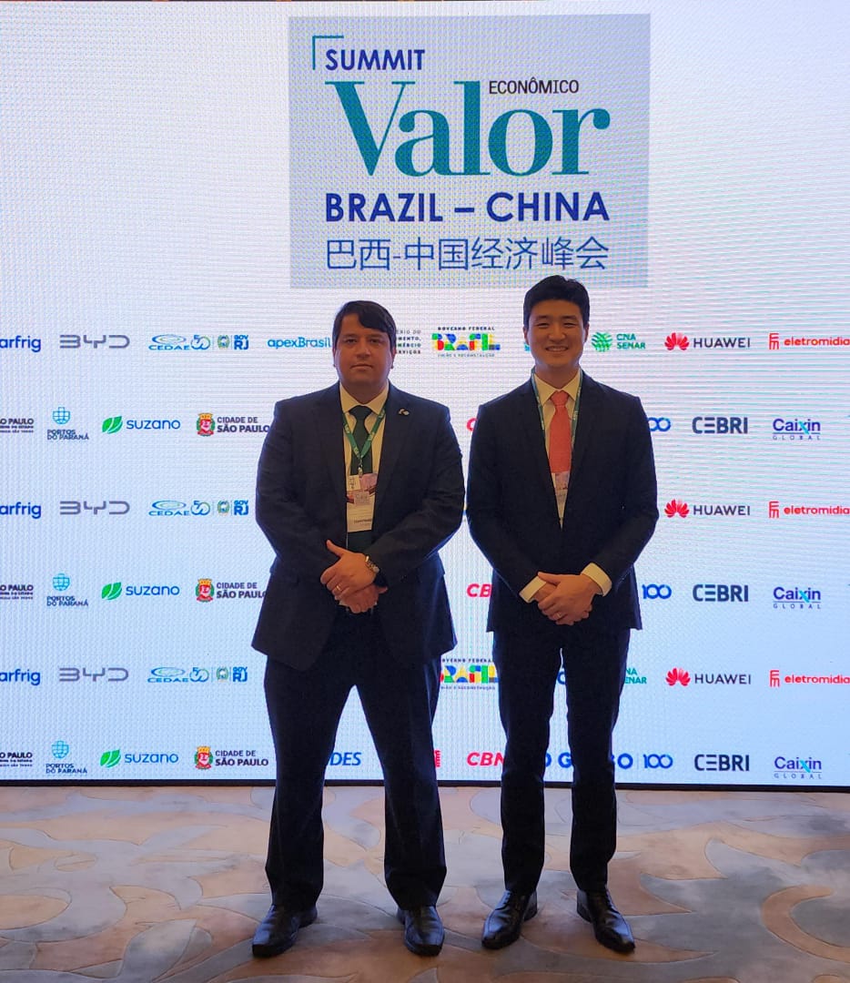 #ParaQuemNaoPodeVer A imagem mostra dois homens de terno em pé, lado a lado, em um evento. O fundo tem um banner com logotipos de várias empresas e as palavras