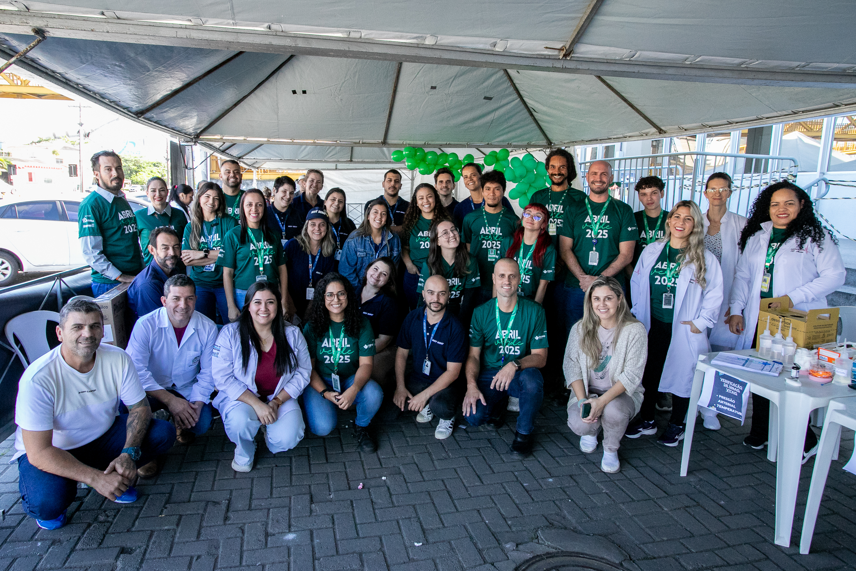 #ParaQuemNaoPodever Um grupo grande de pessoas está posando para uma foto em um ambiente externo. A maioria delas está usando camisetas verdes com a inscrição