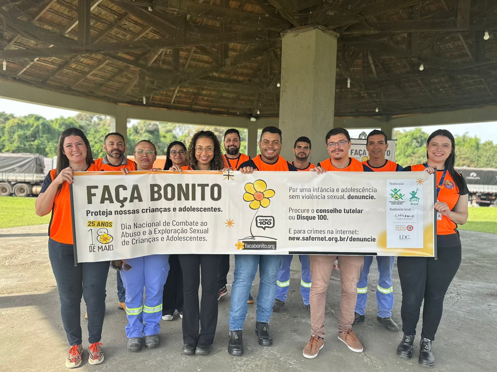 #ParaQuemNaoPodeVer Grupo de pessoas vestindo camisetas laranja posando para uma foto. Eles estão segurando um cartaz que diz: