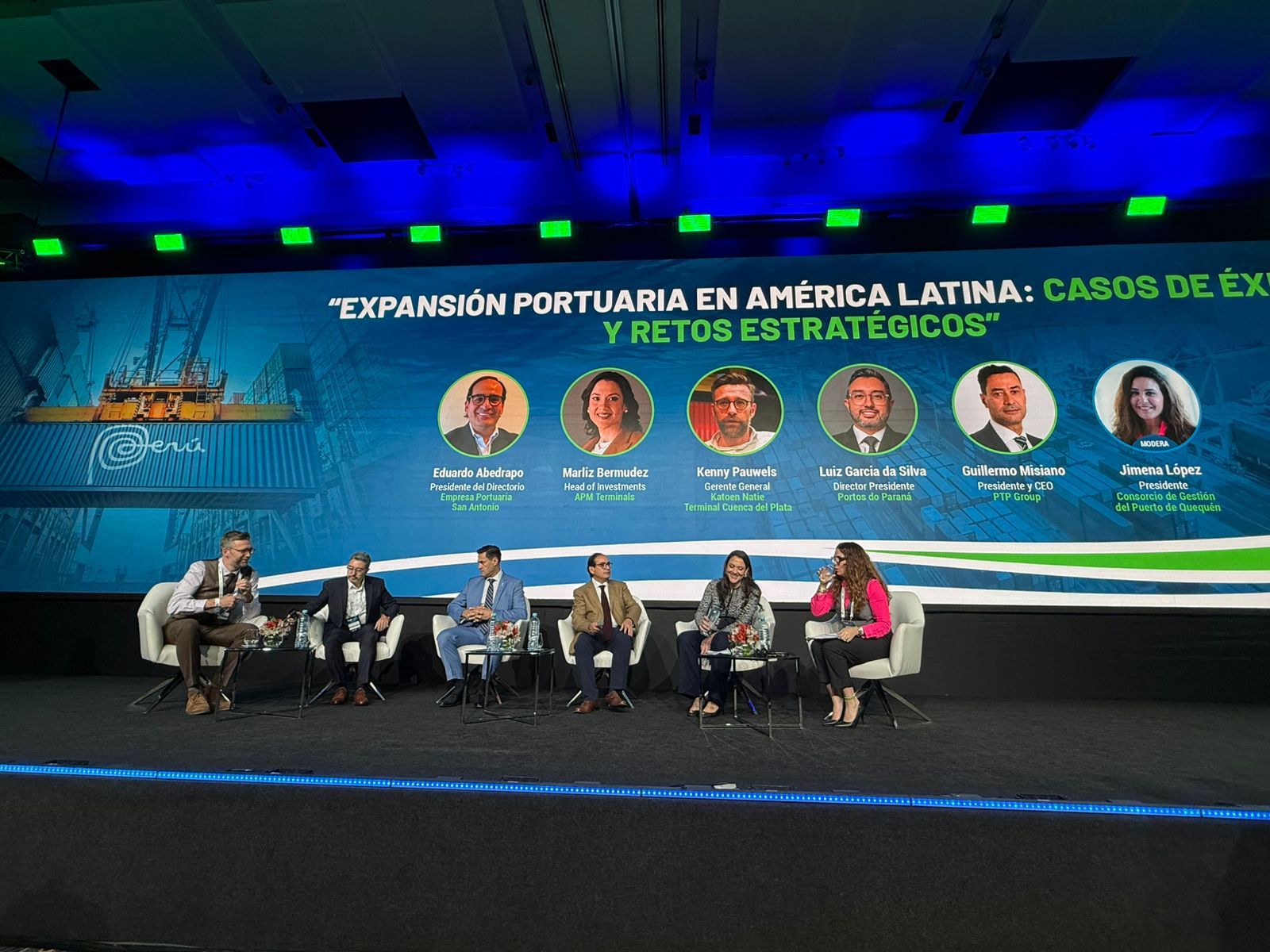 #ParaQuemNaoPodeVer Palco de conferência com seis pessoas sentadas em cadeiras, participando de um painel de discussão. Ao fundo, há um grande painel azul com a imagem de um contêiner portuário e o título do evento em espanhol: