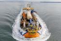 #ParaQuemNaoPodeVer Imagem aérea de um navio em movimento no mar. O navio está cortando a água, criando uma esteira branca ao seu redor. A embarcação possui várias estruturas e equipamentos coloridos em sua parte superior, incluindo elementos em azul, laranja e amarelo.