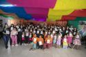 #praquemnaopodever foto mostra um grupo com 50 pessoas segurando um livro com capa branca posando para a foto. Estão em uma sala com parede laranja ao fundo e panos coloridos no teto. Ao fundo, uma um desenho de rosa com o nome 5C ao centro.