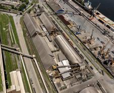 #ParaQuemNaoPodeVer Na imagem, é possível ver várias estruturas grandes, como armazéns ou silos, além de guindastes e outras máquinas pesadas. Há também uma área de cais onde estão atracados navios ou embarcações.