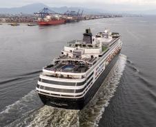 #praquemnaopodever navio de cruzeiros preto e branco cruza a Baía de Paranaguá em direção ao Porto. Na imagem aérea é possível ver o céu nublado e a piscina vazia de um navio que chegou cedo para atracar.