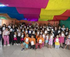 #praquemnaopodever foto mostra um grupo com 50 pessoas segurando um livro com capa branca posando para a foto. Estão em uma sala com parede laranja ao fundo e panos coloridos no teto. Ao fundo, uma um desenho de rosa com o nome 5C ao centro.