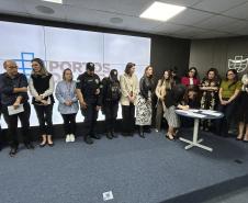 #ParaQuemNaoPodeVer Foto de um grupo de pessoas. São cerca de 19 pessoas, organizadas em duas fileiras, posando para uma foto em um ambiente interno, provavelmente uma sala de reuniões ou auditório. Ao fundo, há um painel com o logotipo e o nome “PORTOS DO PARANÁ”. Há uma mesa redonda branca e azul à frente do grupo. As pessoas estão vestidas de maneira variada, algumas de roupa social, outras de uniforme (aparentando ser de segurança). 