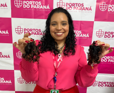 #praquemnaopodever foto mostra mulher negra de camisa rosa segurando uma mecha de cabelo de cada lado e sorrindo em frente de uma parede com os dizeres Portos do Paraná em rosa.