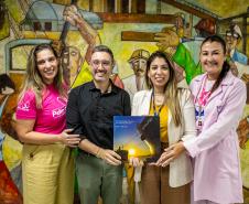 #praquemnaopodever foto mostra quatro pessoas lado a lado, em frente a um mural de trabalhadores, segurando um livro de capa azul e amarela escrito "Porto de Paranáguá - 90 anos"