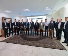 #praquemnaopodever foto mostra 15 homens lado a lado de terno posando para a foto em uma sala de paredes e teto branco, com um tapete de cor escura e um telão ao fundo.