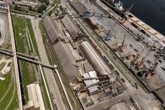 #ParaQuemNaoPodeVer Na imagem, é possível ver várias estruturas grandes, como armazéns ou silos, além de guindastes e outras máquinas pesadas. Há também uma área de cais onde estão atracados navios ou embarcações.