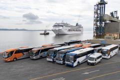 #praquemnaopodever 7 ônibus e uma van estão a frente da foto, no cais do Porto de Paranaguá, aguardando a chegada, atrás, do imponente navio de cruzeiros MSC Armonia. 