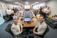 #praquemnaopodever em torno de uma mesa de madeira em formato de u, muitos homens e poucas mulheres posam para a lente da câmera. Eles estão na sala da Portos do Paraná. Com roupas formais, alguns estão sentados, outros em pé, ao fundo aparece o logo Portos do Paraná no telão da exibição.