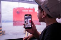 Uma criança está de costas sentada no banco de passageiro de um onibus  gravando os navios atracados no Porto de Paranaguá #praquemnaopodever