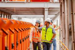 #praquemnaopodever três portuários olham para o lado esquerdo e andam para a frente enquanto conversam dentro de uma coluna de metal. 