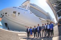 #ParaQuemNaoPodeVer Um grupo de oito pessoas está posando para uma foto em frente a um grande navio de cruzeiro. O navio tem o nome "MSC SEASCAPE" escrito na lateral. As pessoas estão vestidas formalmente, com ternos e camisas sociais. O ambiente parece ser um porto, com o navio atracado ao fundo.