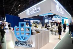 #praquemnaopodever imagem do estande uma feira visto pela ponta. Na frente, em destaque está logo em azul da Portos do Paraná no tamanho de uma pessoa de 1,70m. Ao fundo, banquetas e mesas com pessoas dialogando e em cima o letreiro luminoso escrito "Portos do Paraná".