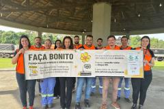 #ParaQuemNaoPodeVer Grupo de pessoas vestindo camisetas laranja posando para uma foto. Eles estão segurando um cartaz que diz: "FAÇA BONITO. Proteja nossas crianças e adolescentes. 25 anos. Dia Nacional de Combate ao Abuso e à Exploração Sexual de Crianças e Adolescentes". O cartaz também menciona o Disque 100 e fala sobre a importância de proteger crianças e adolescentes. Ao fundo, há uma estrutura coberta e uma área verde.
