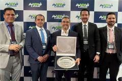 #ParaQuemNaoPodeVer Foto de cinco homens de terno, posando para uma foto em frente a um painel com o logo “ANDAV LATAM”. Eles estão sorrindo e segurando um quadro e um troféu, sugerindo que receberam algum tipo de prêmio ou reconhecimento. O ambiente parece ser um evento corporativo ou uma premiação.