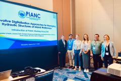 #praquemnaopodever na foto aparecem seis pessoas em pé, posadas, juntas e ao lado de um telão escrito PIANC. Ao fundo, a parede bege da sala de reunião.