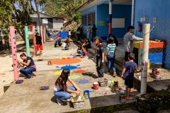 #praquemnaopodever imagem aerea do patio de uma escola pequena a beira mar cheia de crianças e adolescentes pintando o chão e a parede com desenhos de peixes e caranguejos.