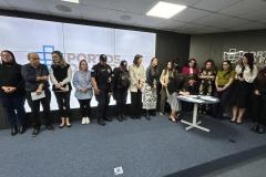#ParaQuemNaoPodeVer Foto de um grupo de pessoas. São cerca de 19 pessoas, organizadas em duas fileiras, posando para uma foto em um ambiente interno, provavelmente uma sala de reuniões ou auditório. Ao fundo, há um painel com o logotipo e o nome “PORTOS DO PARANÁ”. Há uma mesa redonda branca e azul à frente do grupo. As pessoas estão vestidas de maneira variada, algumas de roupa social, outras de uniforme (aparentando ser de segurança). 
