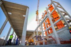 #praquemnaopodever foto do chão do canteiro de obras do Moegão, com os pilares cinzas e máquinas laranjas, trabalhadores estão no local espalhados trabalhando e o céu está de fundo, em um azul claro.