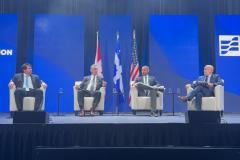 #praquemnaopodever foto mostra quatro homens brancos de terno sentados em poltronas brancas individuais em um palco com fundo azul e três bandeiras atrás.