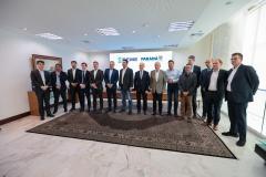 #praquemnaopodever foto mostra 15 homens lado a lado de terno posando para a foto em uma sala de paredes e teto branco, com um tapete de cor escura e um telão ao fundo.