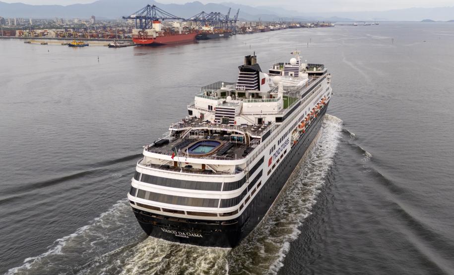 #praquemnaopodever navio de cruzeiros preto e branco cruza a Baía de Paranaguá em direção ao Porto. Na imagem aérea é possível ver o céu nublado e a piscina vazia de um navio que chegou cedo para atracar.