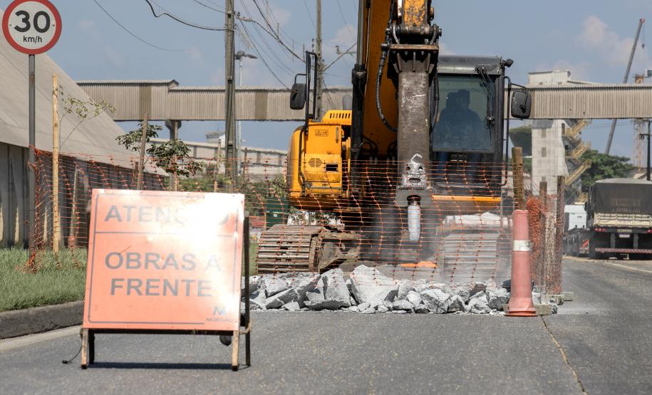 #ParaQuemNaoPodeVer A foto exibe uma obra na rua. Na imagem, há uma placa de aviso com o texto "ATENÇÃO OBRAS À FRENTE". Ao fundo, é possível ver uma escavadeira amarela e uma cerca de proteção laranja. No canto superior direito, há uma placa de trânsito indicando o limite de velocidade de 30 km/h. A cena parece estar em uma área urbana com calçadas e postes de eletricidade.