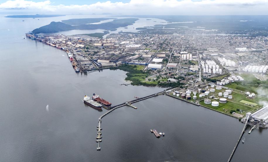#praquemnaopodever em meio a Baía de Paranaguá, está um píer com dois navios atracados. Ao fundo, várias casas e empresas que foram a área portuária. As nuvens cobrem a cidade
