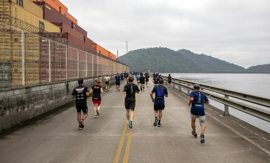 #praquemnaopodever vários corredores aparecem de costas cruzando o cais, pelas margens do Porto de Paranaguá. À direita, aparecem as aguas da baía de Paranaguá, ao fundo as ilhas cobertas de árvores e à esquerda os contêineres amarelos, vermelhos e laranjas.