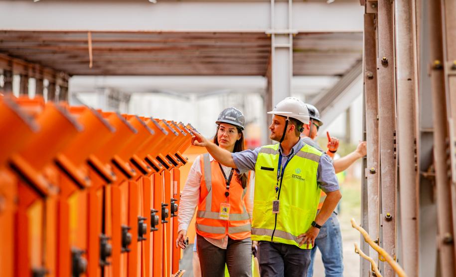 #praquemnaopodever três portuários olham para o lado esquerdo e andam para a frente enquanto conversam dentro de uma coluna de metal.
