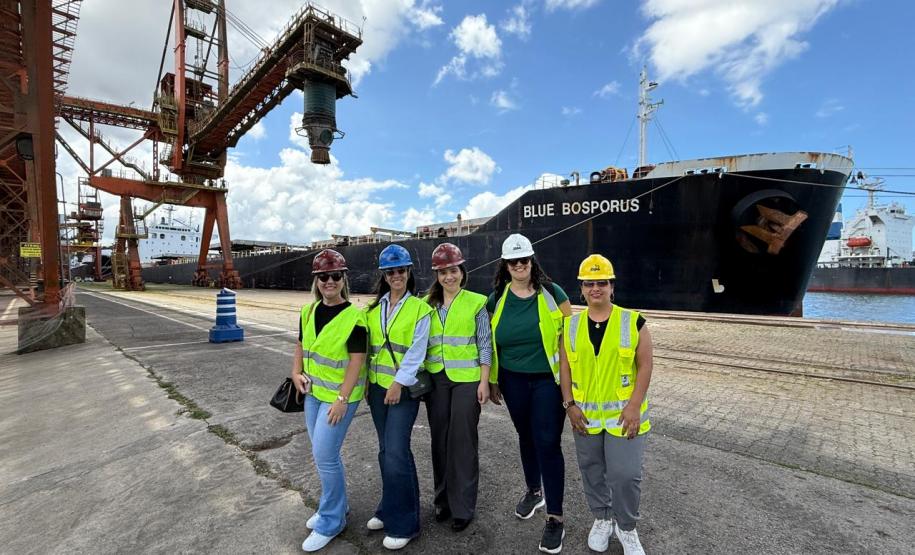 #praquemnaopodever cinco mulheres posam lado a lado no cais do Porto de Santos. Trajando coletes amarelos luminescentes, camisas por baixo e calças jeans, todas estão com capacetes e sorriem para a foto.