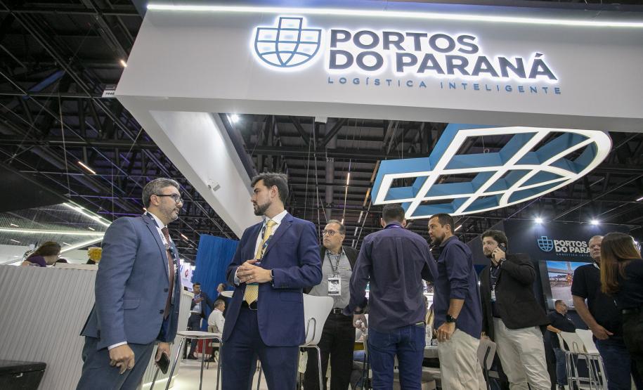 dois homens cnversam em frente ao estande da Intermodal no evento. Ao fundo pessoas circulam plo estande.