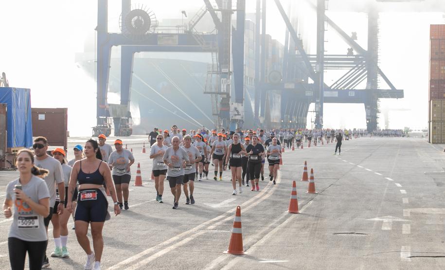 #praquemnaopodever foto mostra multidao de atletas atravessando o cais de um porto correndo. Ao fundo, a neblina encobre metade de um navio. Os guindastes gigantes azuis estão ao lado da embarcação, mas sem se moverem.