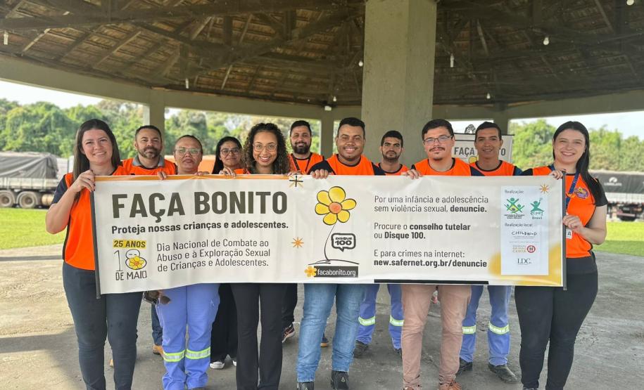 #ParaQuemNaoPodeVer Grupo de pessoas vestindo camisetas laranja posando para uma foto. Eles estão segurando um cartaz que diz: "FAÇA BONITO. Proteja nossas crianças e adolescentes. 25 anos. Dia Nacional de Combate ao Abuso e à Exploração Sexual de Crianças e Adolescentes". O cartaz também menciona o Disque 100 e fala sobre a importância de proteger crianças e adolescentes. Ao fundo, há uma estrutura coberta e uma área verde.