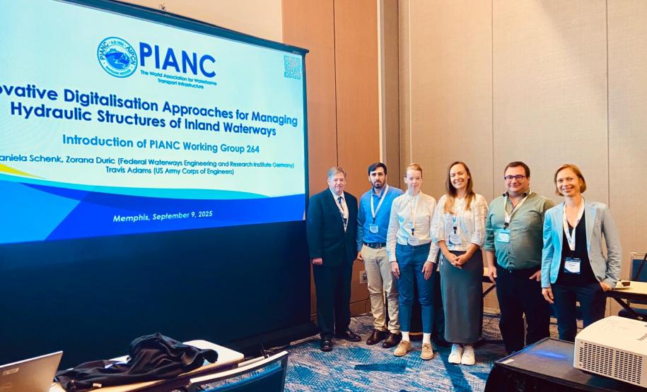 #praquemnaopodever na foto aparecem seis pessoas em pé, posadas, juntas e ao lado de um telão escrito PIANC. Ao fundo, a parede bege da sala de reunião.