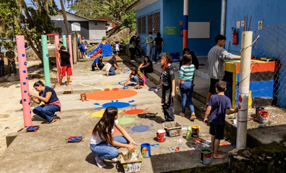 #praquemnaopodever imagem aerea do patio de uma escola pequena a beira mar cheia de crianças e adolescentes pintando o chão e a parede com desenhos de peixes e caranguejos.