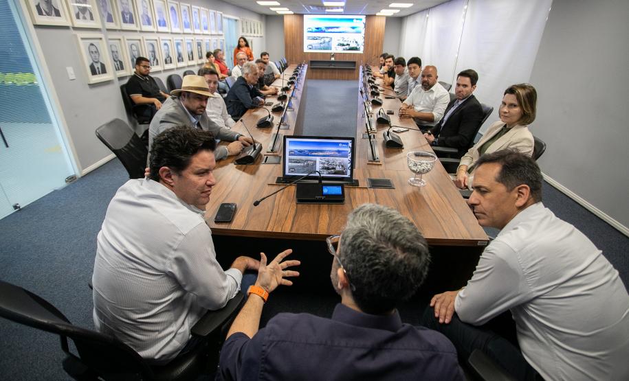 #praquemnaopodever foto mostra um homem sentado de costas para a camera, na ponta de uma mesa em formato de u e rodeado de pessoas sentadas com roupas formais olhando para ele.