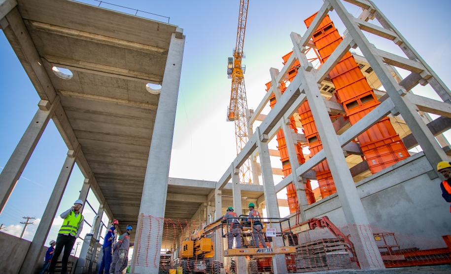 #praquemnaopodever foto do chão do canteiro de obras do Moegão, com os pilares cinzas e máquinas laranjas, trabalhadores estão no local espalhados trabalhando e o céu está de fundo, em um azul claro.