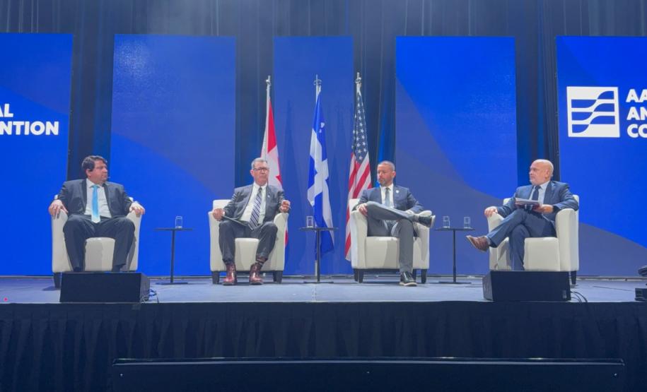 #praquemnaopodever foto mostra quatro homens brancos de terno sentados em poltronas brancas individuais em um palco com fundo azul e três bandeiras atrás.