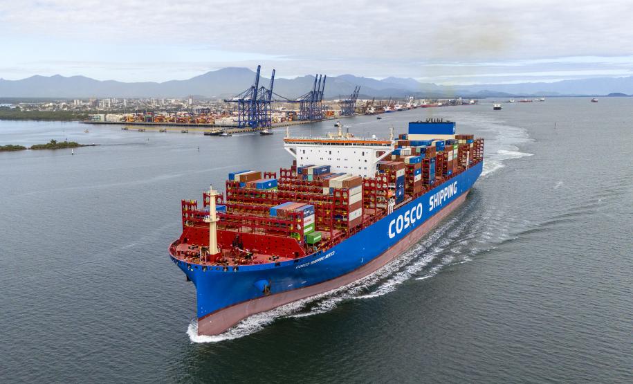 #praquemnaopodever foto aérea mostra navio metade vermelho metade azul, lotado de contêineres cruzando a Baía de Paranaguá deixando uma esteira de espuma, com o cais do Porto de Paranaguá ao fundo.