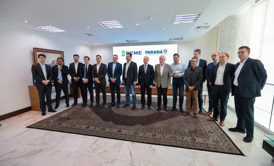 #praquemnaopodever foto mostra 15 homens lado a lado de terno posando para a foto em uma sala de paredes e teto branco, com um tapete de cor escura e um telão ao fundo.