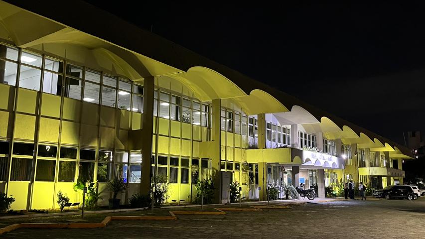 #ParaQuemNaoPodeVer Imagem exibe uma fotografia de um prédio iluminado à noite. O prédio tem uma fachada com muitas janelas e está iluminado com luzes amarelas, criando um efeito visual marcante. A imagem está inclinada, mostrando a lateral do prédio, que parece ter uma arquitetura moderna com formas curvas.